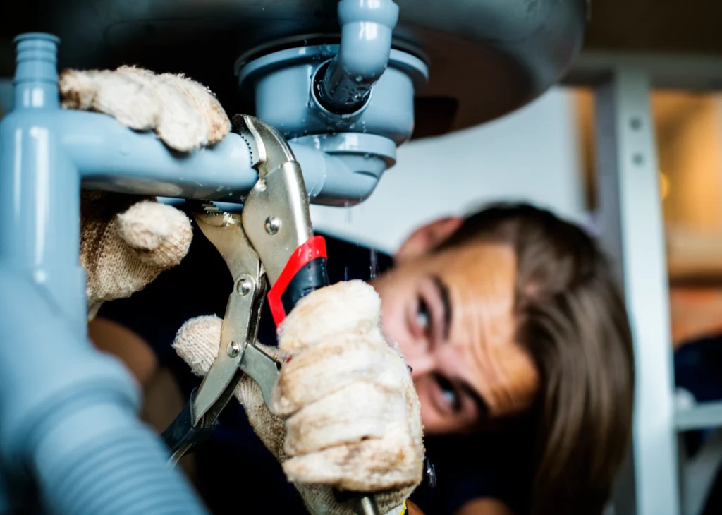 A man tightening the pipe under the kitchen sink.