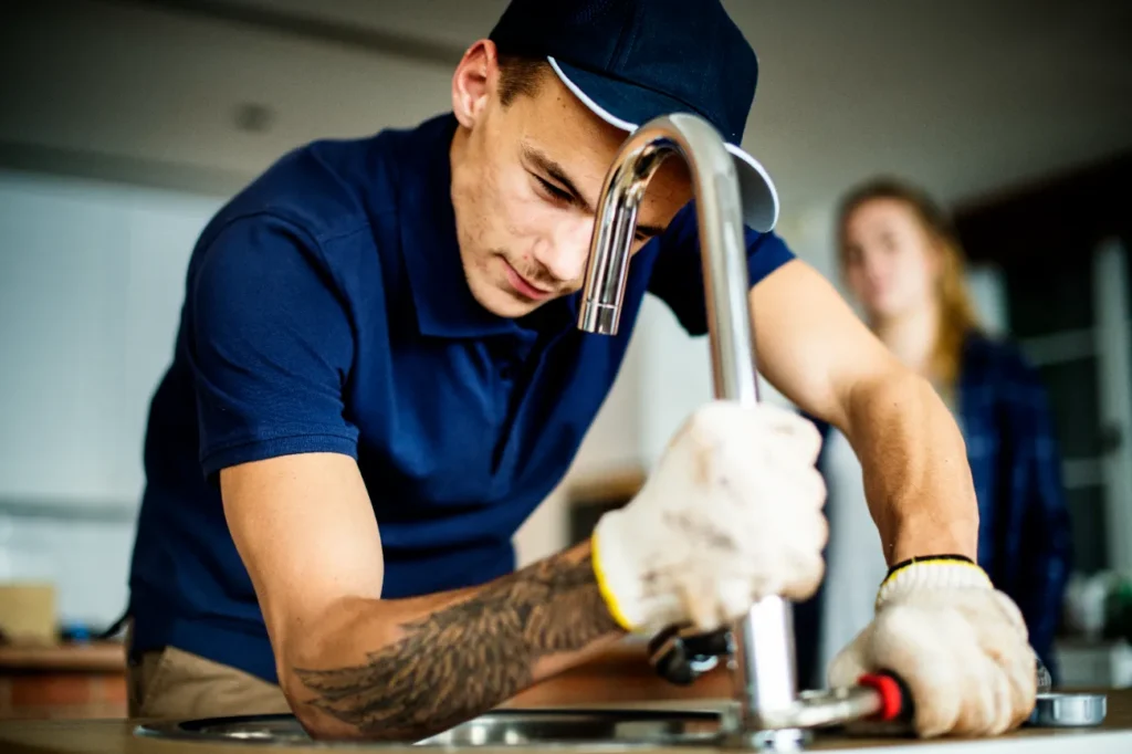 A plumber installing the faucet on the kitchen sink.